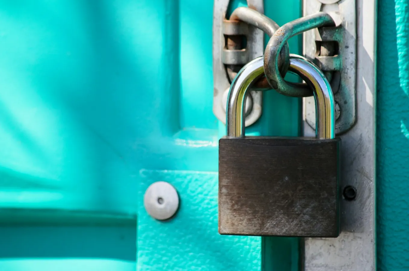 Photo: a padlock hanging from the latch of a bright turquoise metal door.